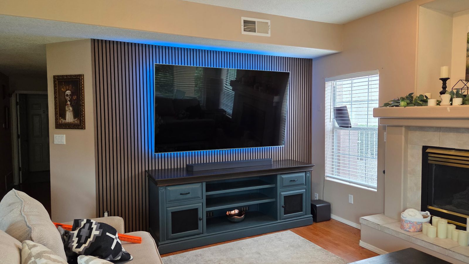 Large TV mounted on a wood slat accent wall with blue backlighting, centered above a media console
